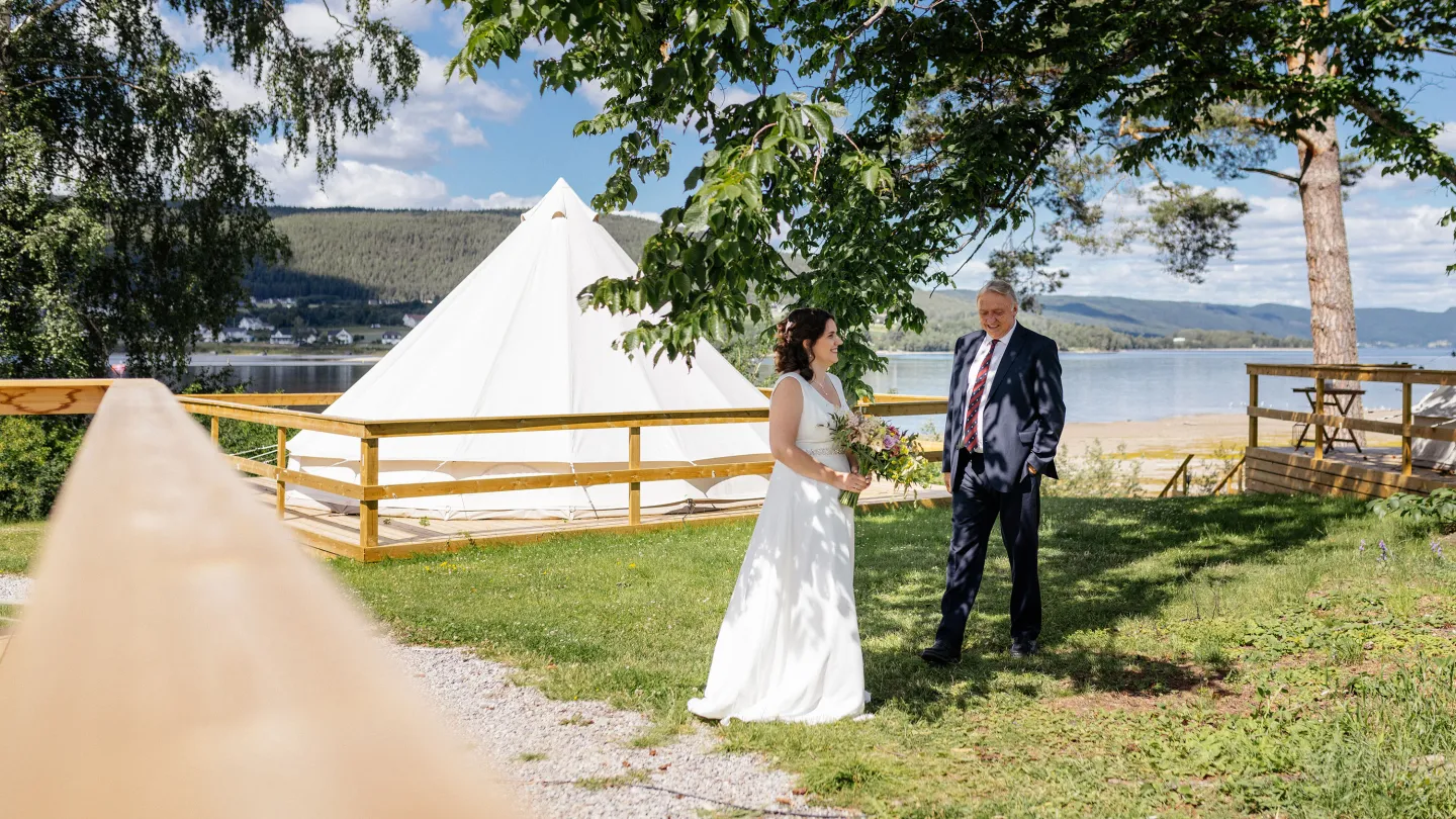 Brud med bukett snakker med far ved innsjøen